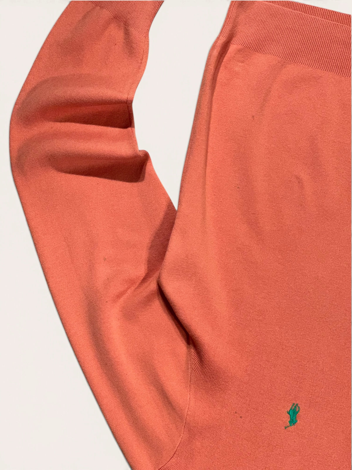 Détail de la maille et d’une manche du pull Ralph Lauren orange, avec logo vert et petites taches.