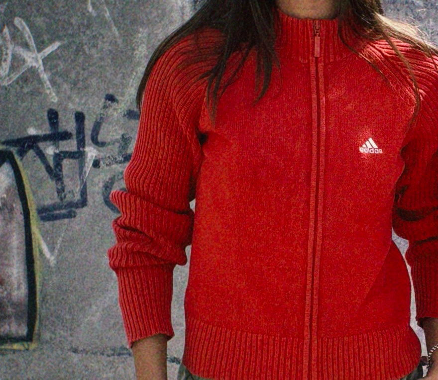 Pull rouge Adidas devant un mur graffiti